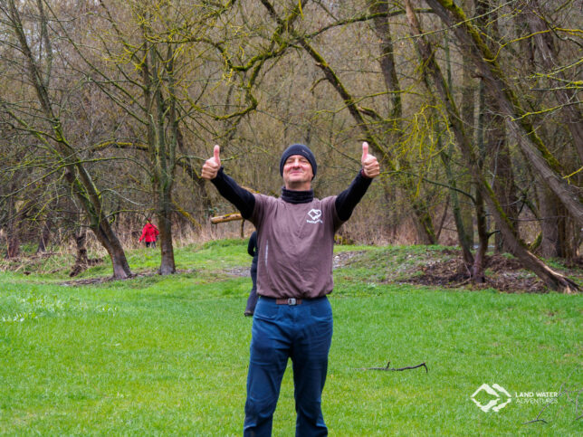 Eine Person auf einer Wiese stehend, lachend beide Daumen in die Luft haltend