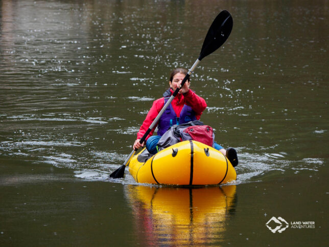 Eine Frau in einem gelben Packraft mit violetter Schwimmweste quert die Nahe.