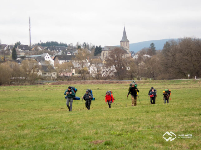 Bepackte Packrafter auf einer Wiese auf dem Weg zum Fluss