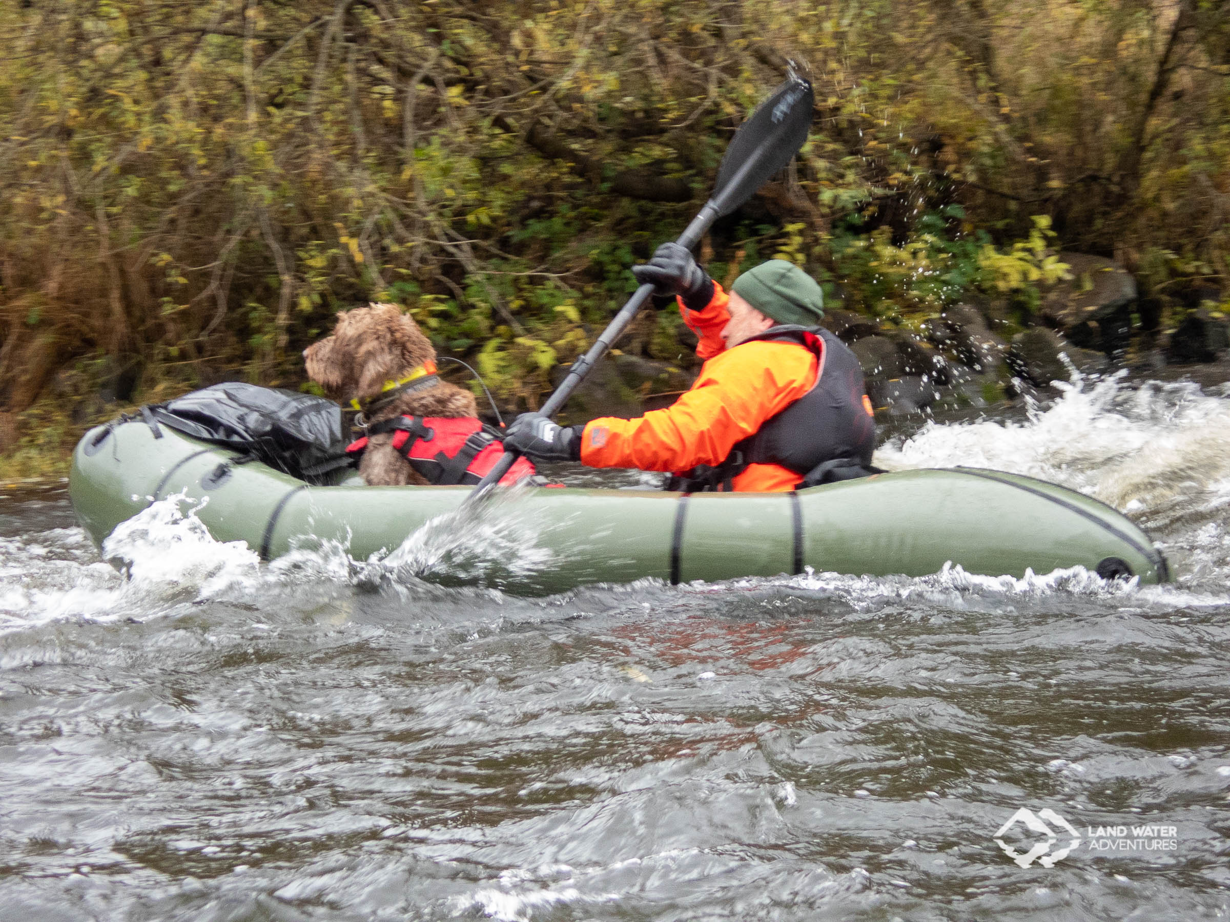 Ein grünes Packraft mit Hund und Paddler rauscht durch eine Welle der Nahe