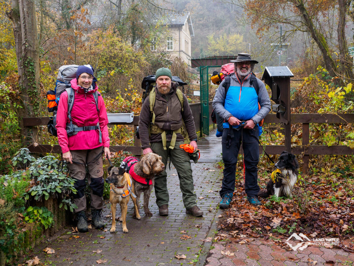 Drei Packrafter mit Hunden und großen Rucksäcken