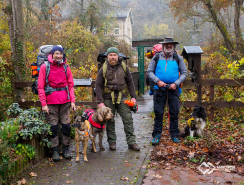 Drei Packrafter mit Hunden und großen Rucksäcken