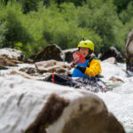 Lächelnde Packrafterin paddelt zwischen den Felsblöcken der Soca hindurch
