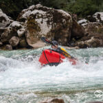 Ein rotes Packraft stößt durch die Welle der Soca